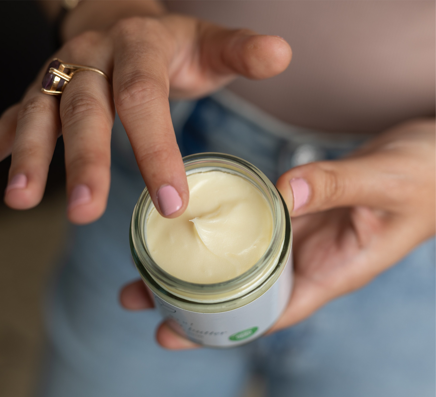 A person who is holding the shea + cocoa body butter and displaying the texture of the cream