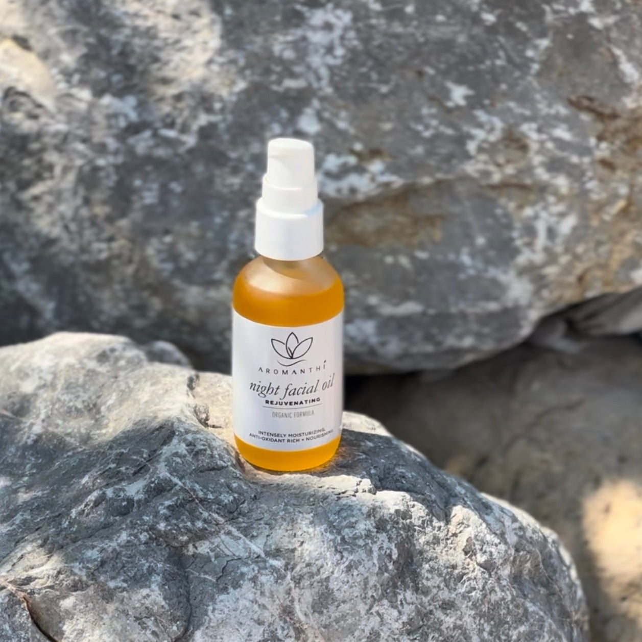 The night facial oil resting on a marble boulder with the sun shining on it