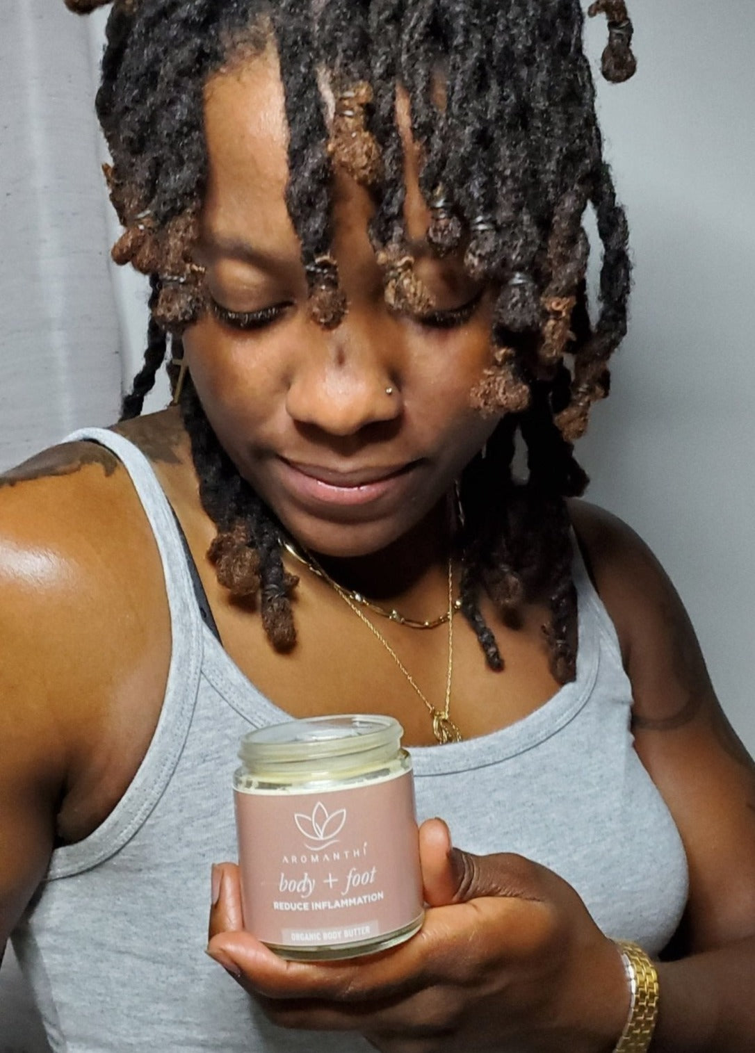 A woman who is looking down and holding a jar of Aromanthi body and foot whipped body butter
