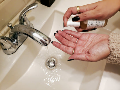 A photo of a bathroom sink with running water and a woman about to add a pump of facial wash to her hands as she prepares her skincare routine