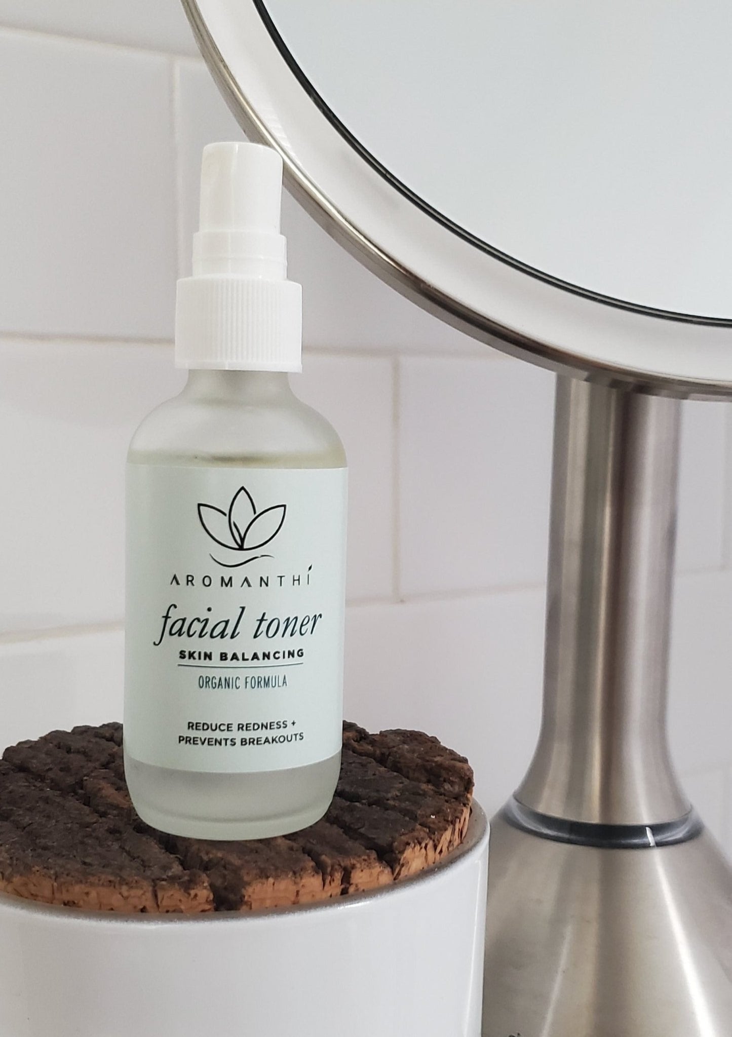 An background of white tile with the image of facial toner next to a silver mirror