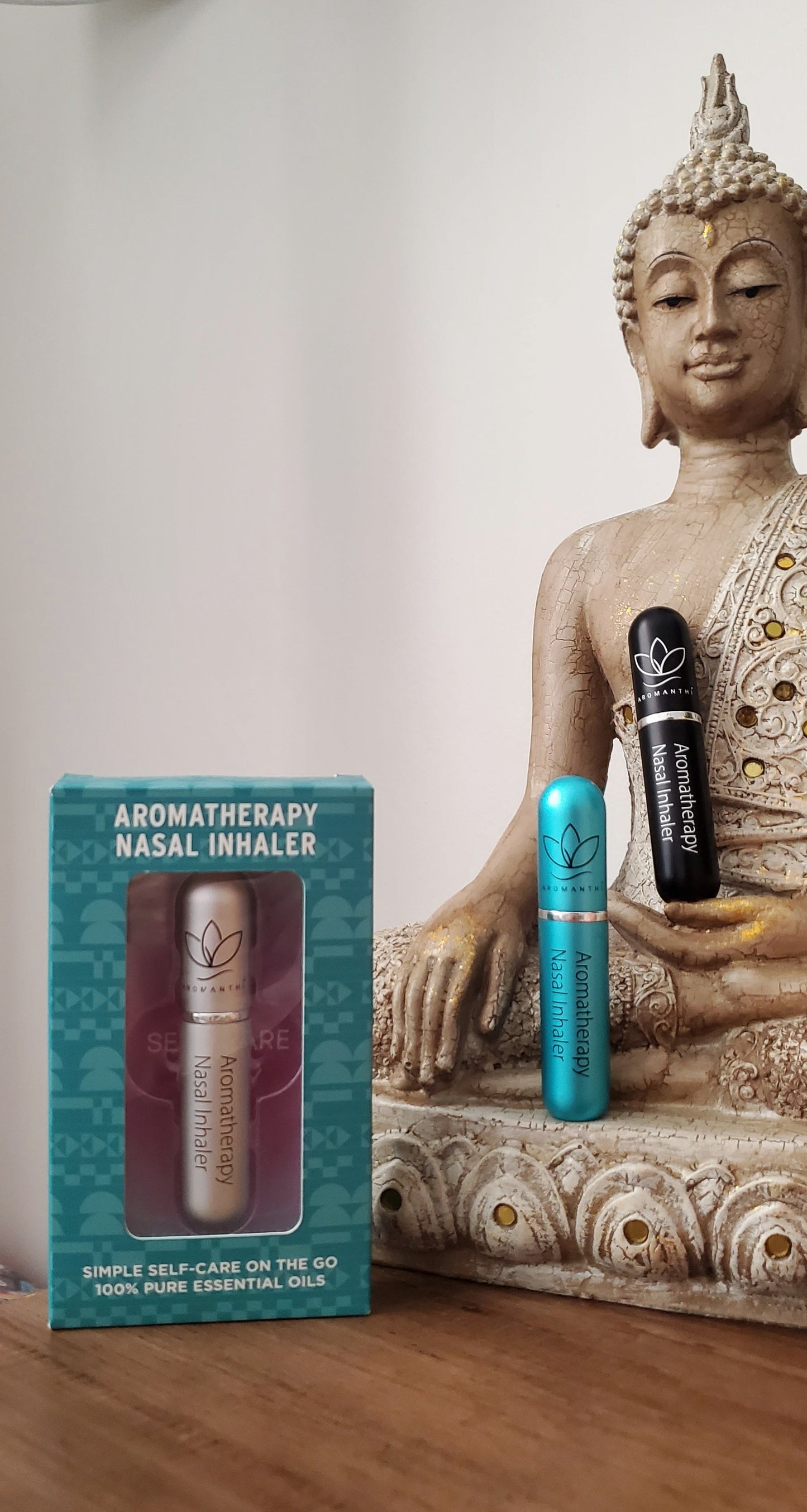 A buddha statue displayed in the background of a white wall with 3 inhaler choices placed along the statue