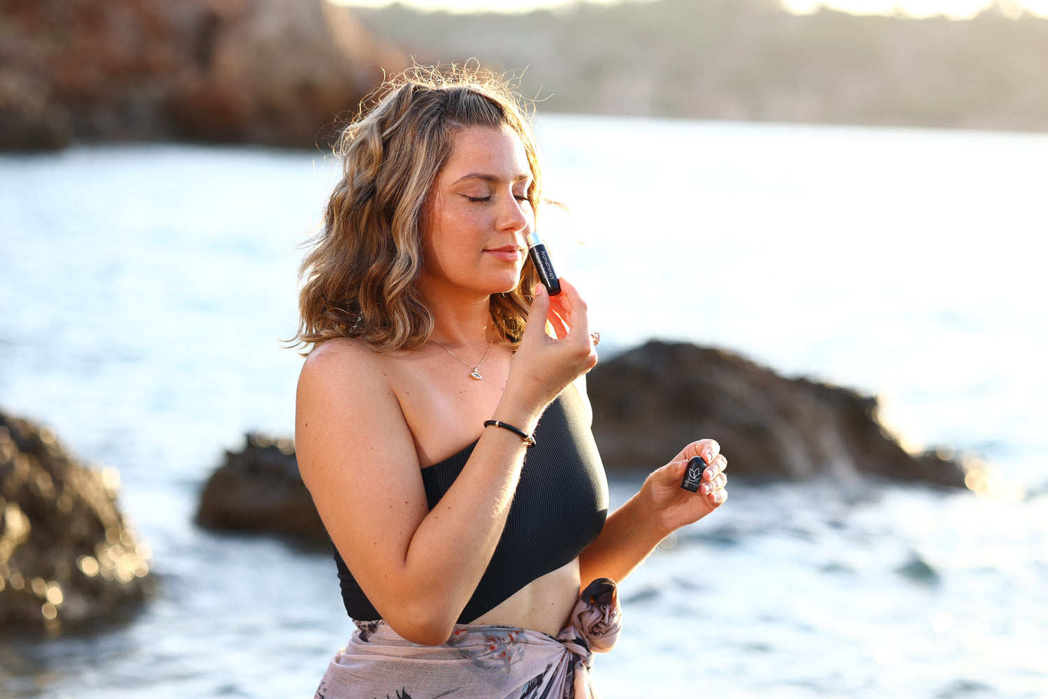 A woman who is at the beach and sniffing her inhaler that's in the color black