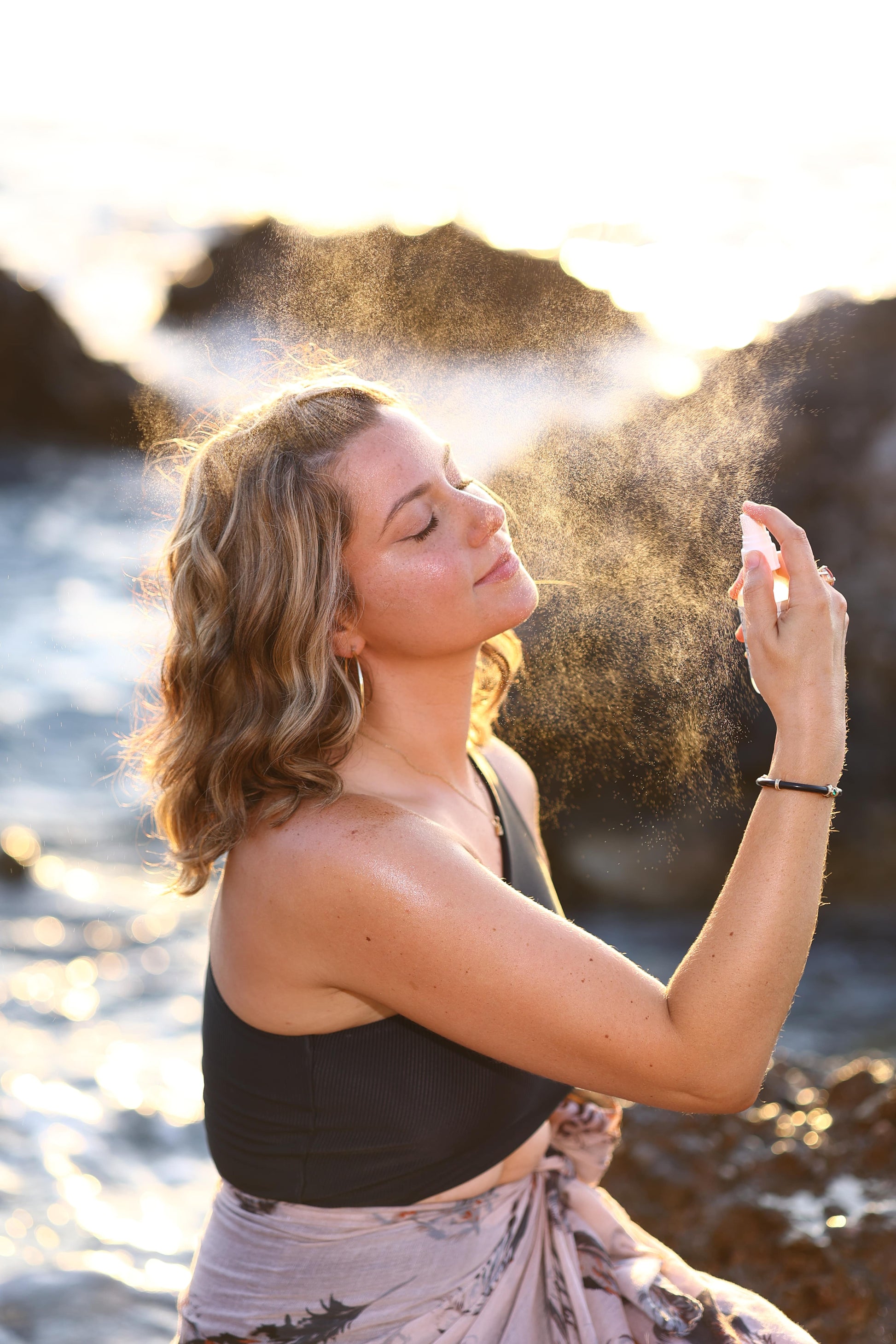 A woman who is at the beach and applying the facial toner spray on her face