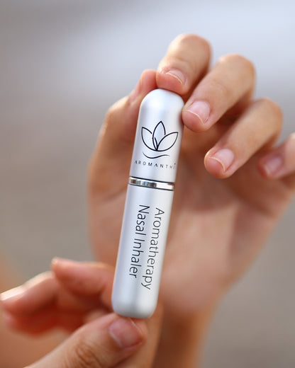 Aromanthi's Aromatherapy nasal inhaler held in a hand with a blurred background. Inhaler is the silver color option
