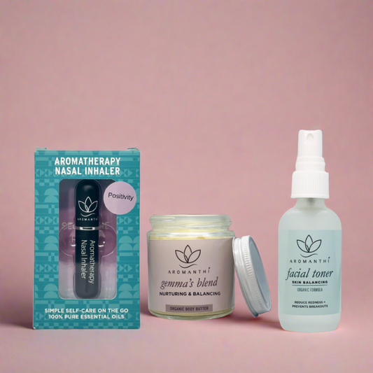 A pink backdrop with 3 Aromanthi aromatherapy products that are in the pms self care bundle which include gemma's blend body butter, facial toner, and positivity blend for aromatherapy nasal inhaler. All 3 products are organic.