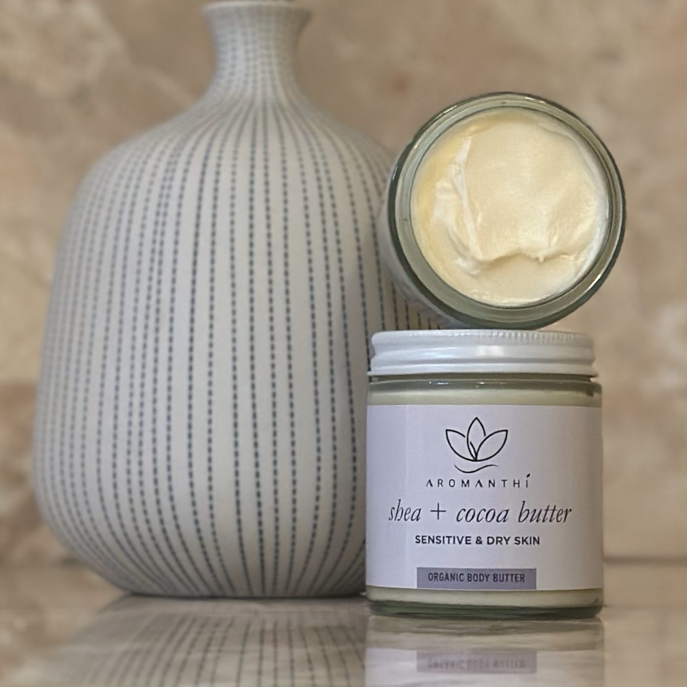 A marble backdrop with a white and blue vase which features the shea and cocoa butter jar, and texture of the whipped formula