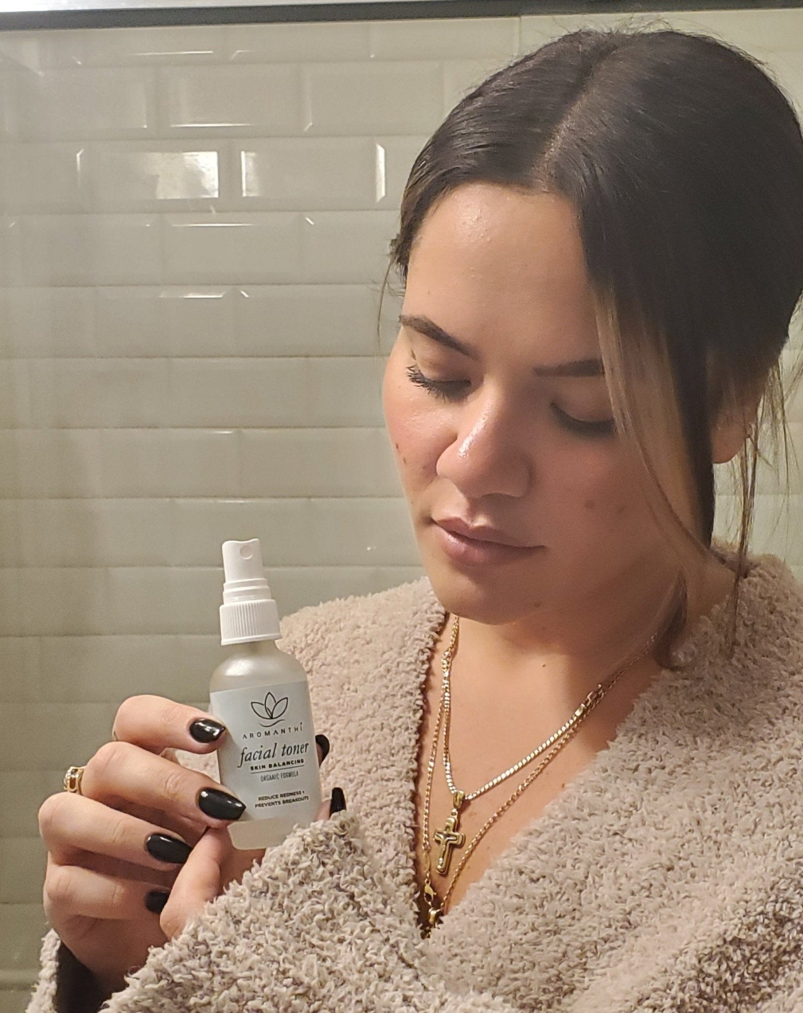 A woman in a bathroom setting holding and looing down at the Aromanthi facial toner 