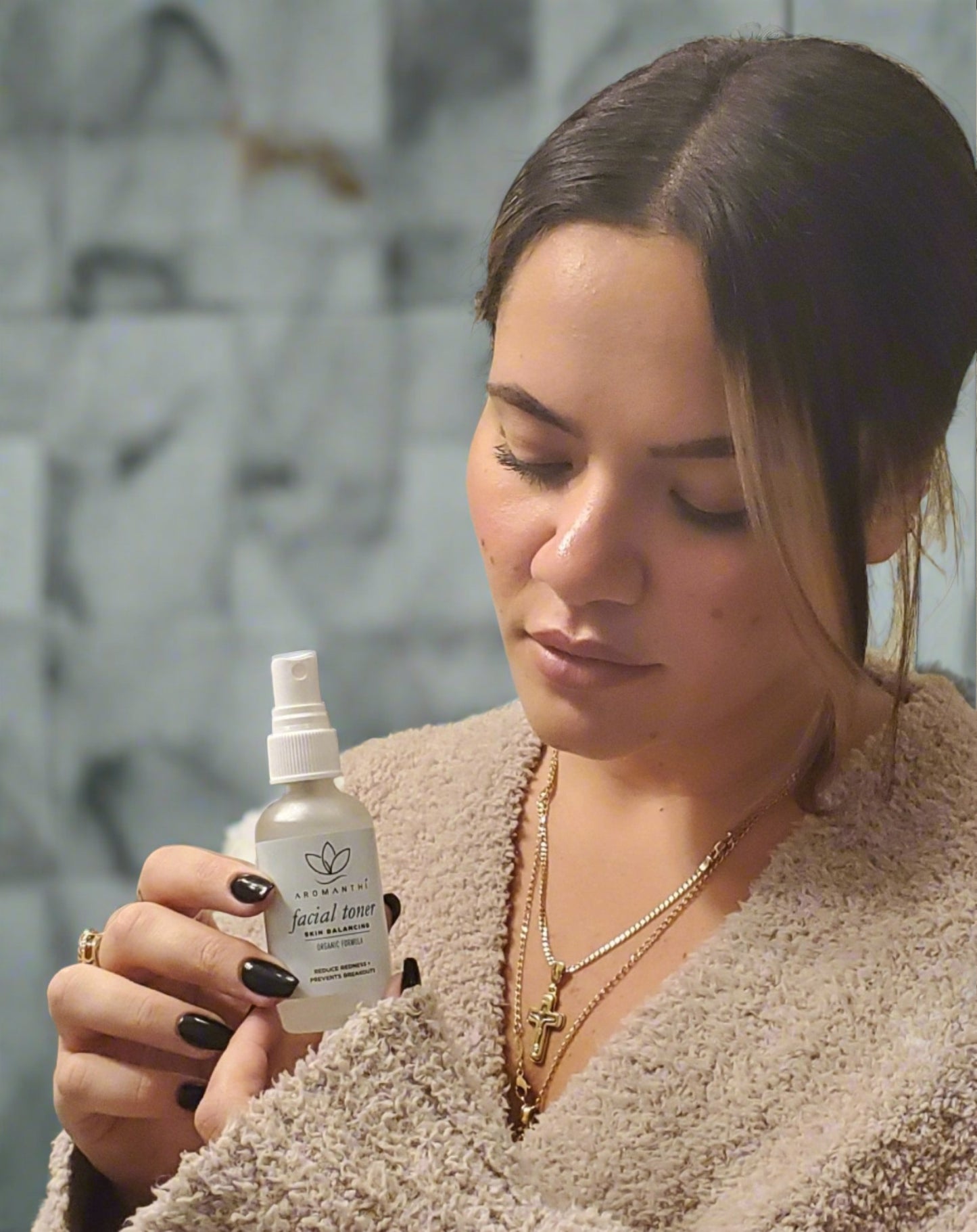A woman in a bathroom setting holding and looing down at the Aromanthi facial toner 