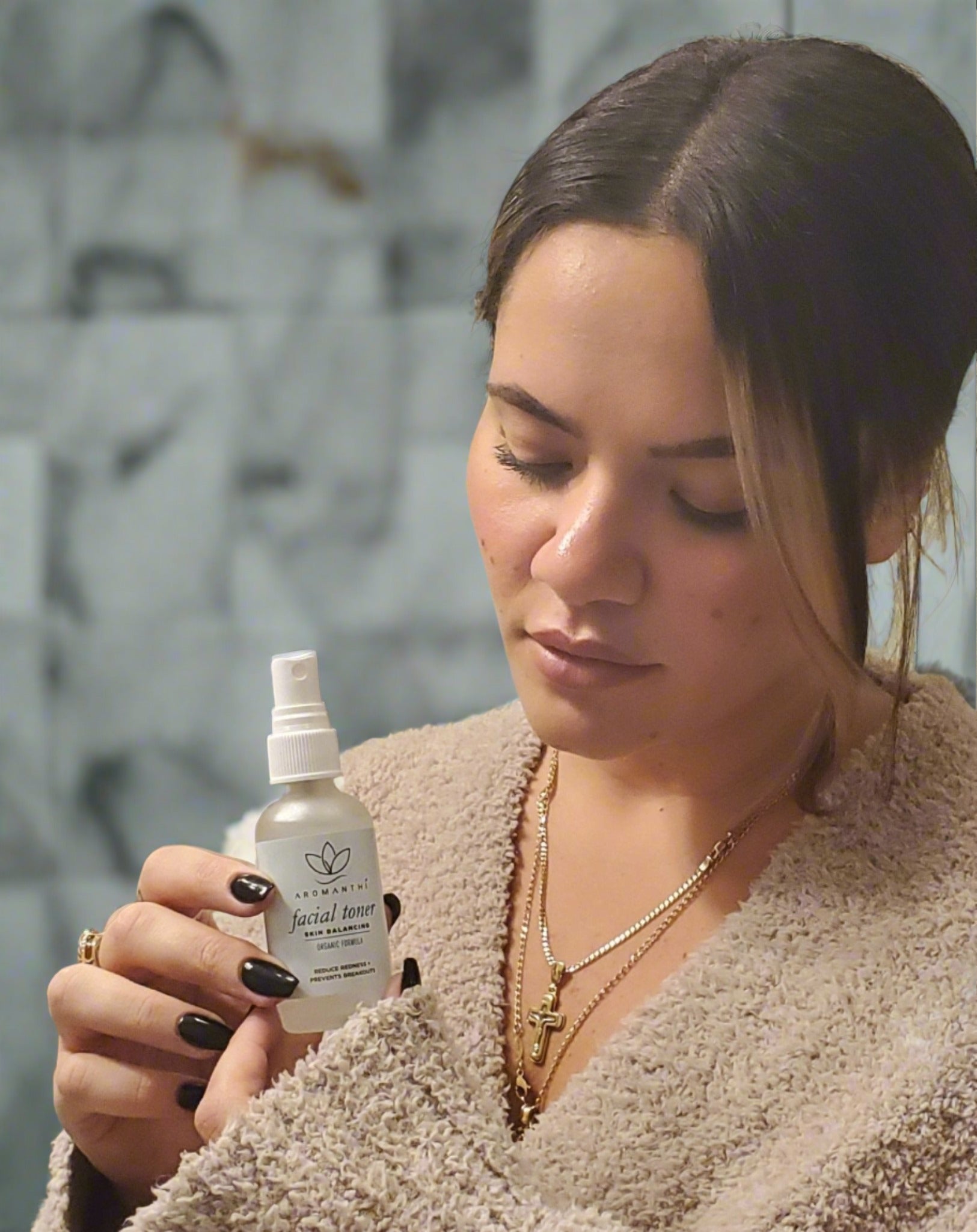 A woman in a bathroom setting holding and looing down at the Aromanthi facial toner 