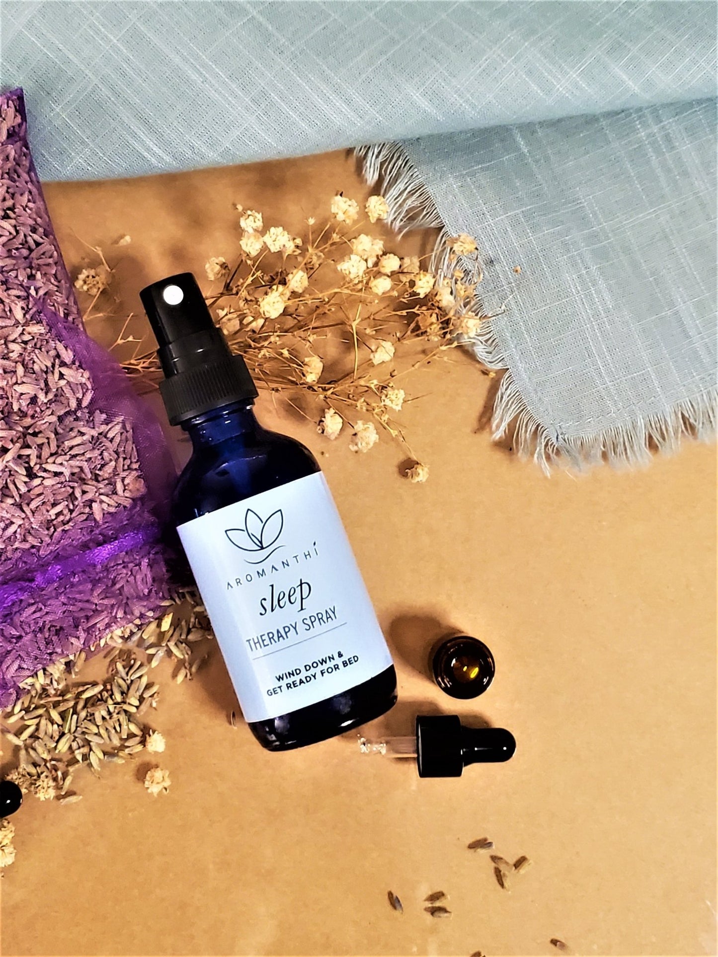 Sleep Therapy Spray laying against a tan backdrop surrounded by dry chamomile and lavender flower petals