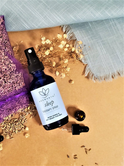 Sleep Therapy Spray laying against a tan backdrop surrounded by dry chamomile and lavender flower petals