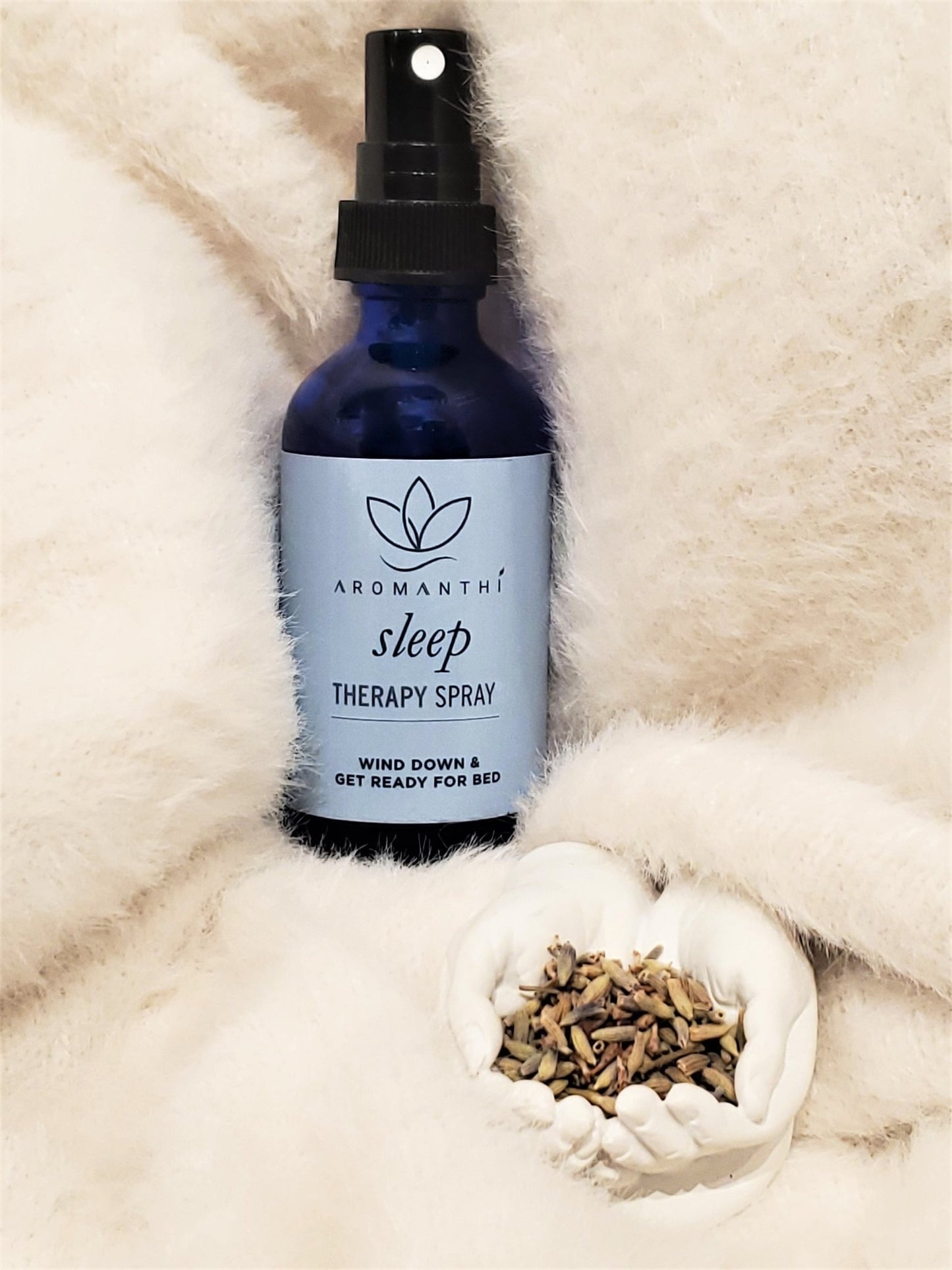 A white blanket backdrop with the sleep therapy spray and a small container of lavender petals