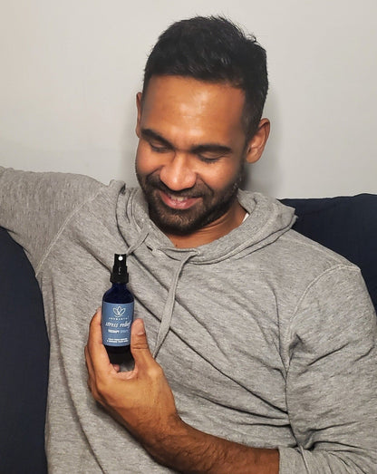 A man looking down and smiling as he is holding a bottle of stress relief aromatherapy spray